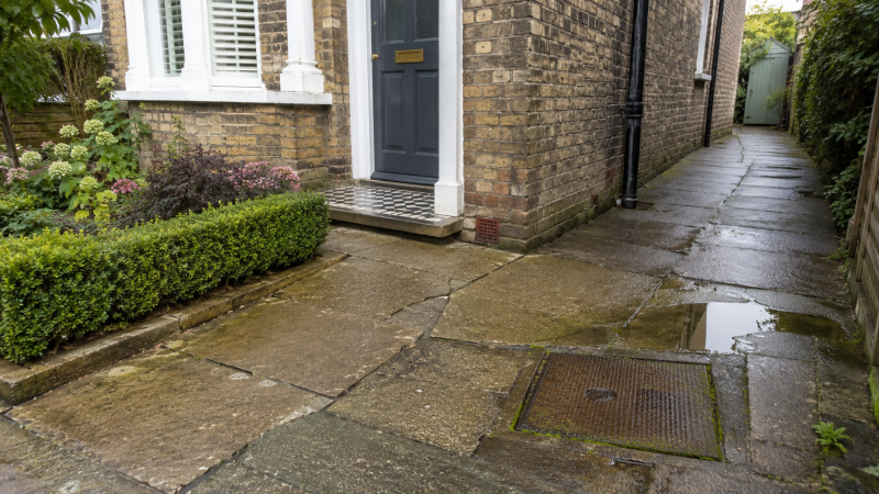 Twickenham home exterior with damp paving, an inspection chamber and subtle signs of drain pipe movement near the property.